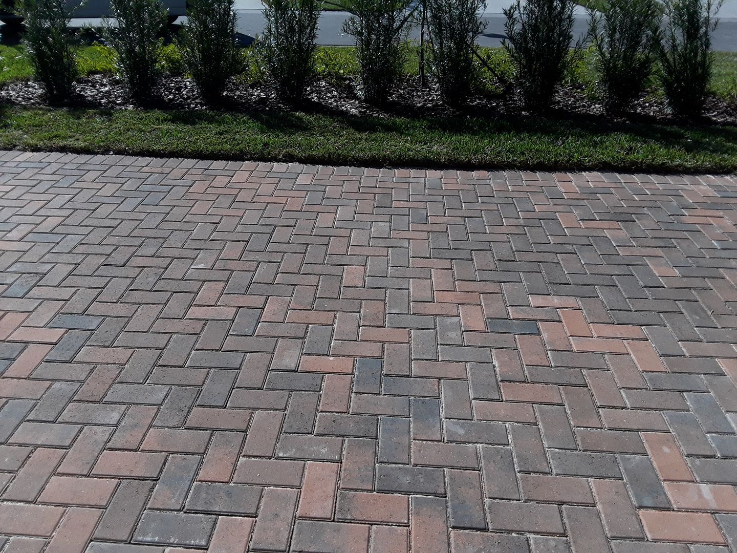 Herringbone brick driveway with grass border and hedge backdrop.