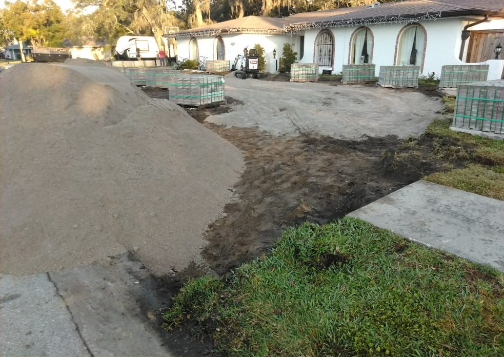 A large pile of sand beside a house; construction materials and a partially excavated driveway.