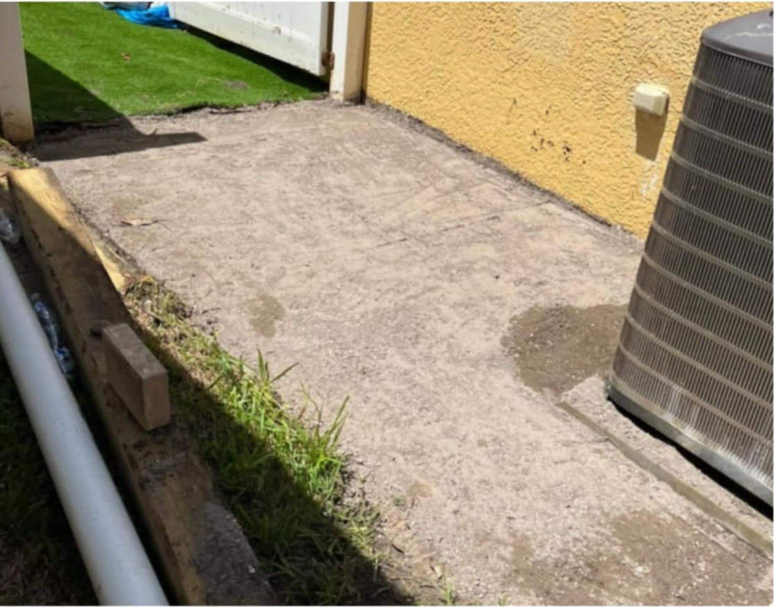 Concrete walkway beside a yellow wall, adjacent to an air conditioning unit.