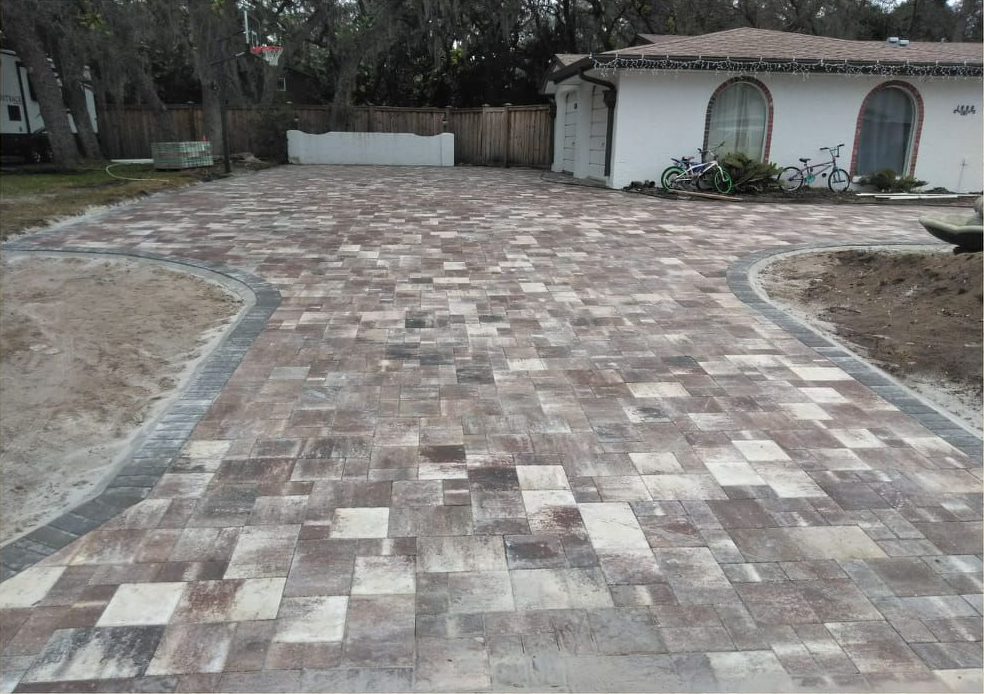 Brick driveway in mottled earth tones leads to a white stucco house with arched windows and bicycles parked in front.