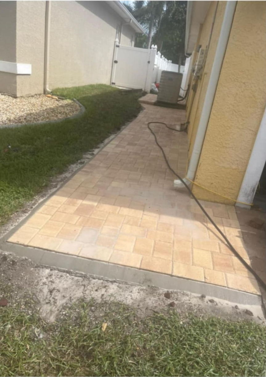 Pathway paved with light brown bricks next to green grass and a cream-colored building.