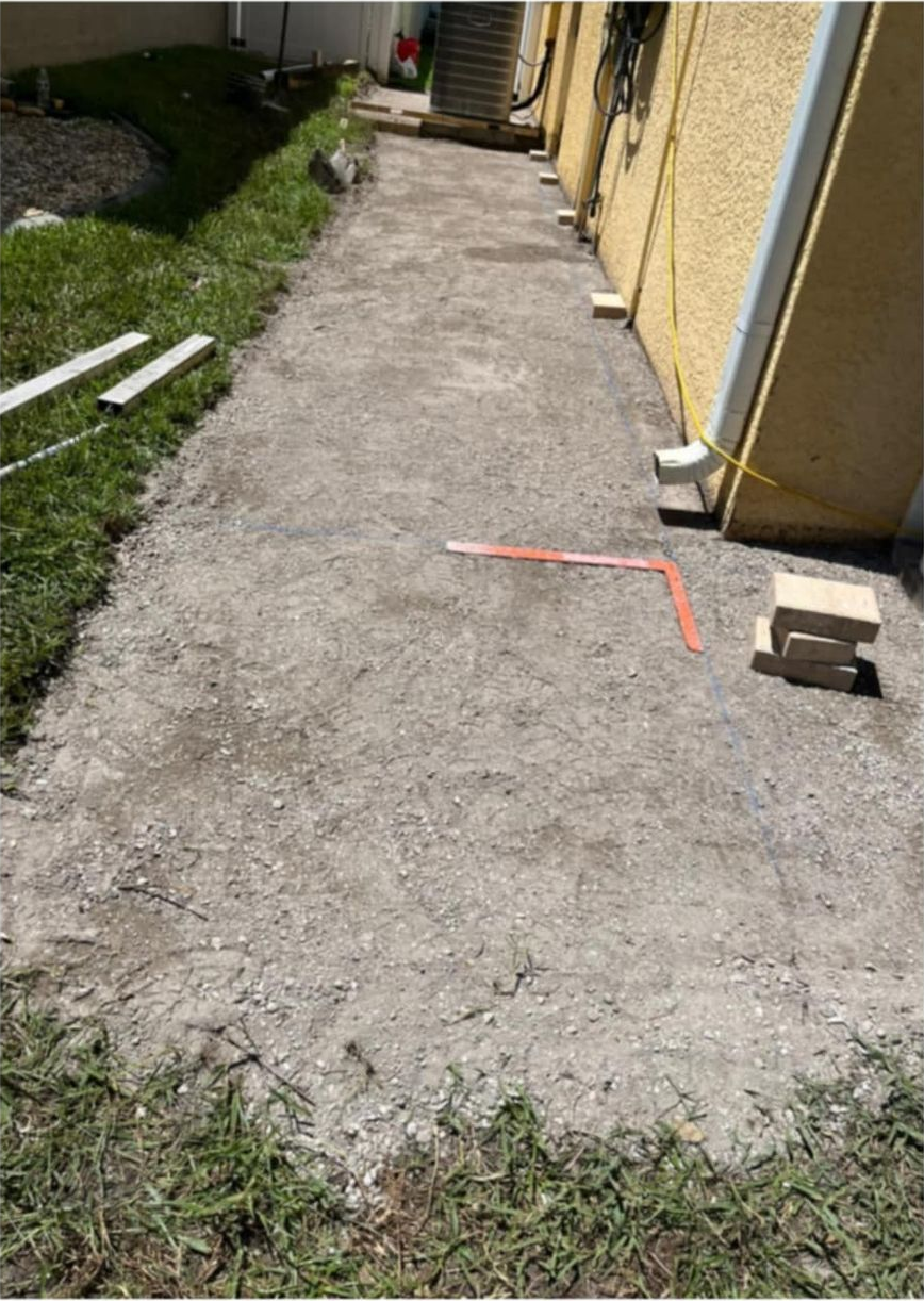 Gravel path next to a yellow building. Grass borders the path. Wooden blocks and tools are present.