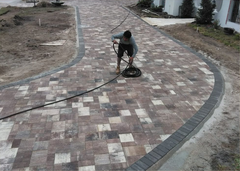 Person pressure washing a brick driveway.