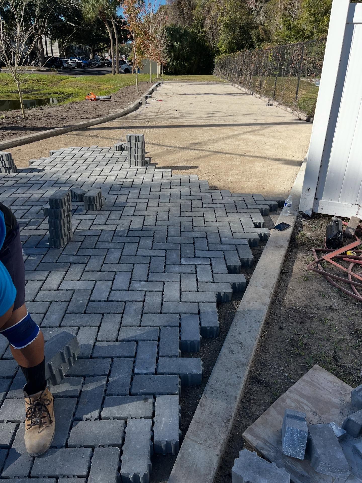 Person laying gray brick pavers on a pathway.