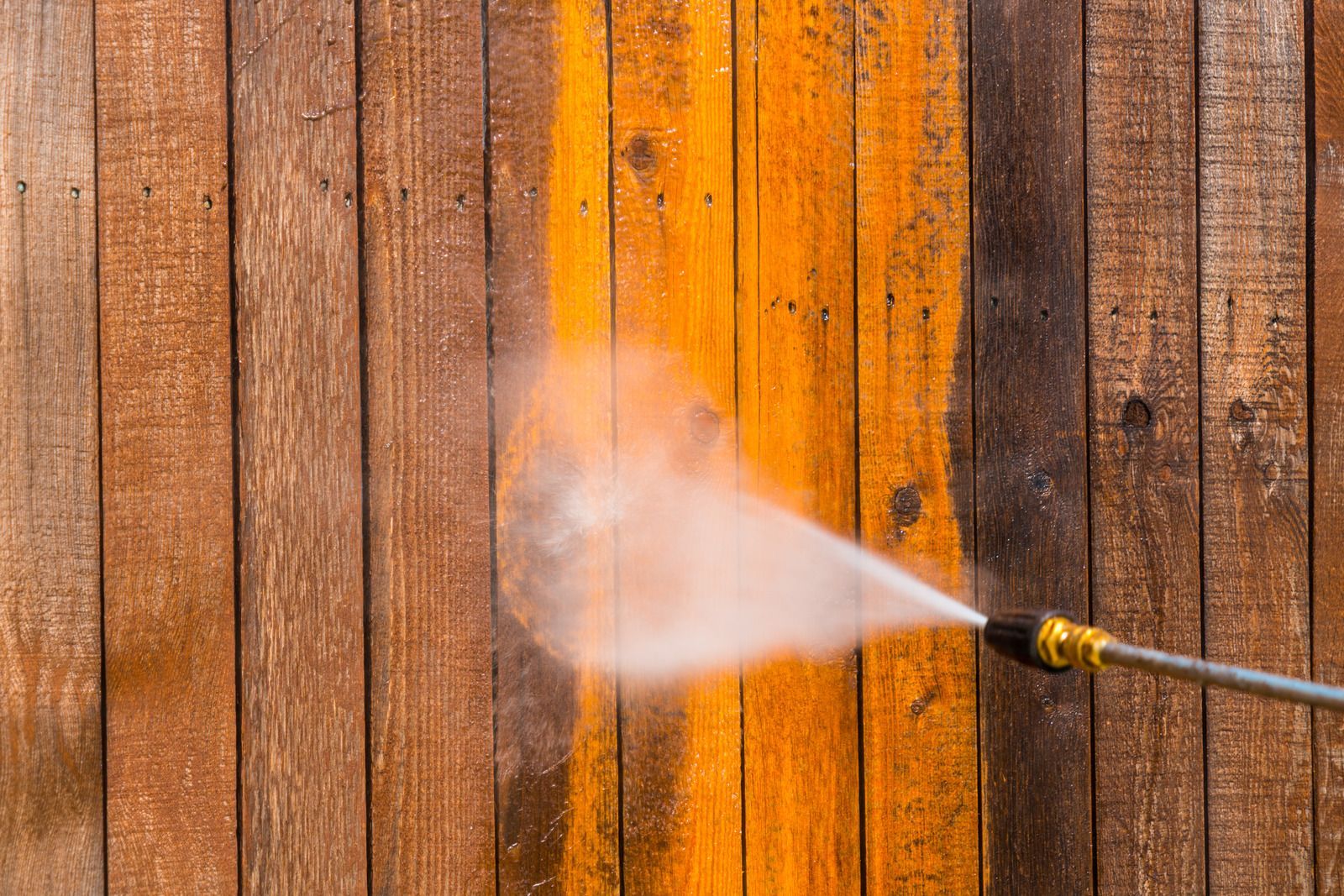 Pressure washer cleaning wooden planks. Brown wood, water spray, exterior, bright.