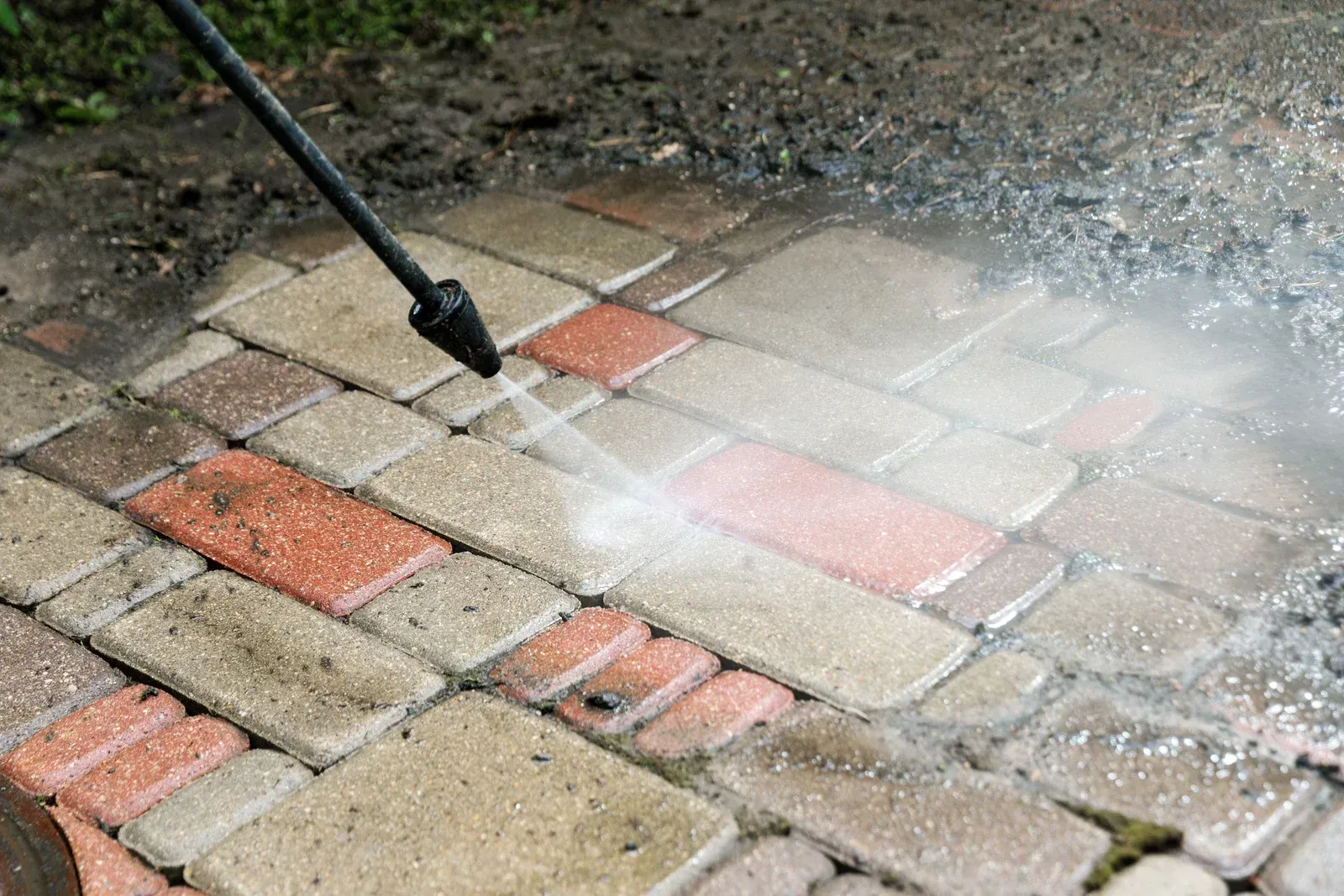 Pressure washer spraying water onto a brick patio, cleaning the surface.