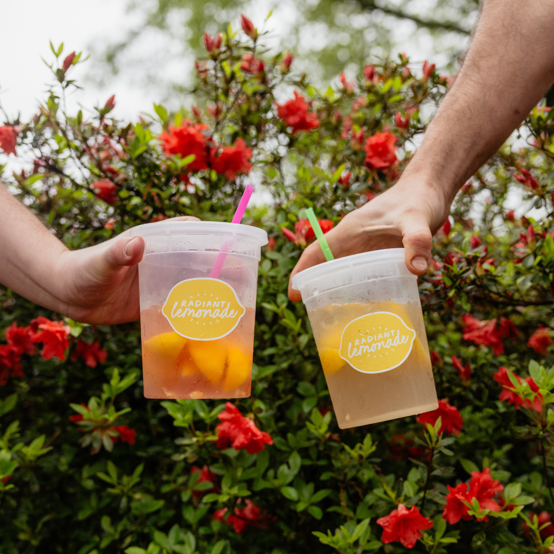 A person is holding three cups of lemonade with straws.