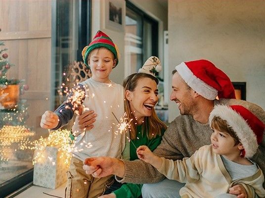 Una famiglia è seduta sul davanzale di una finestra con in mano delle fontane luminose.