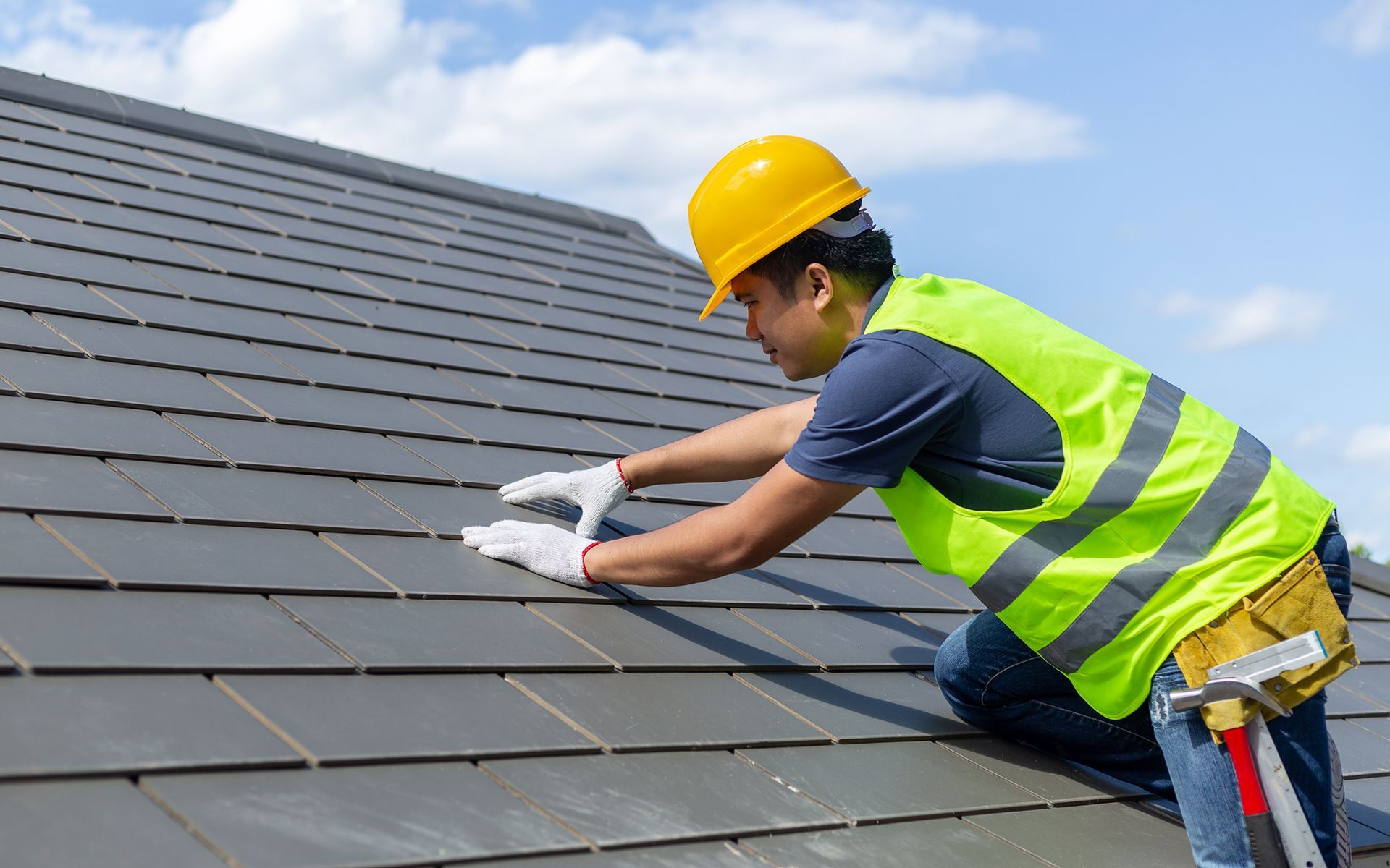 A man wearing a hard hat and safety vest is working on a roof.