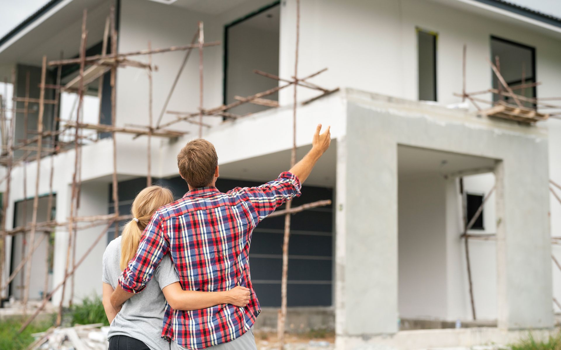A man and a woman are standing in front of a house under construction.