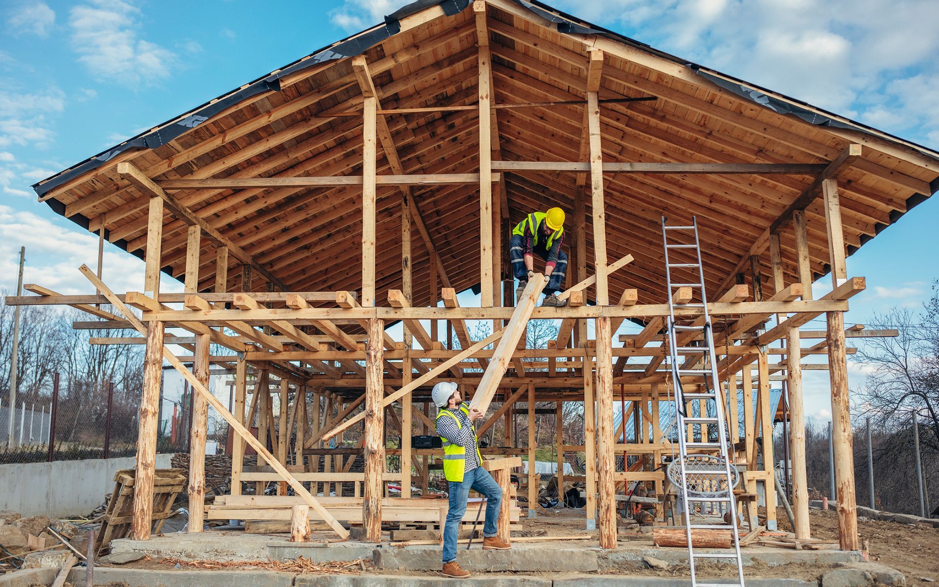 A man is standing in front of a wooden house under construction.