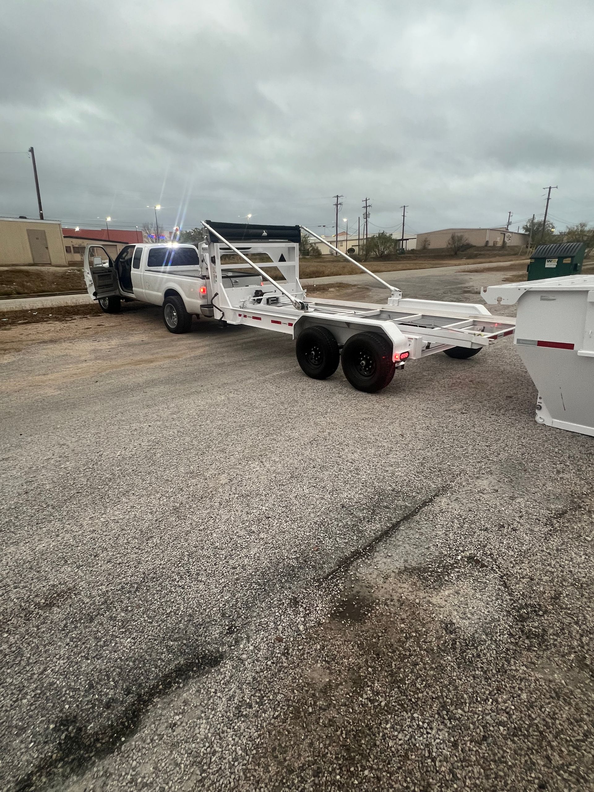 A truck is towing a trailer in a gravel lot.