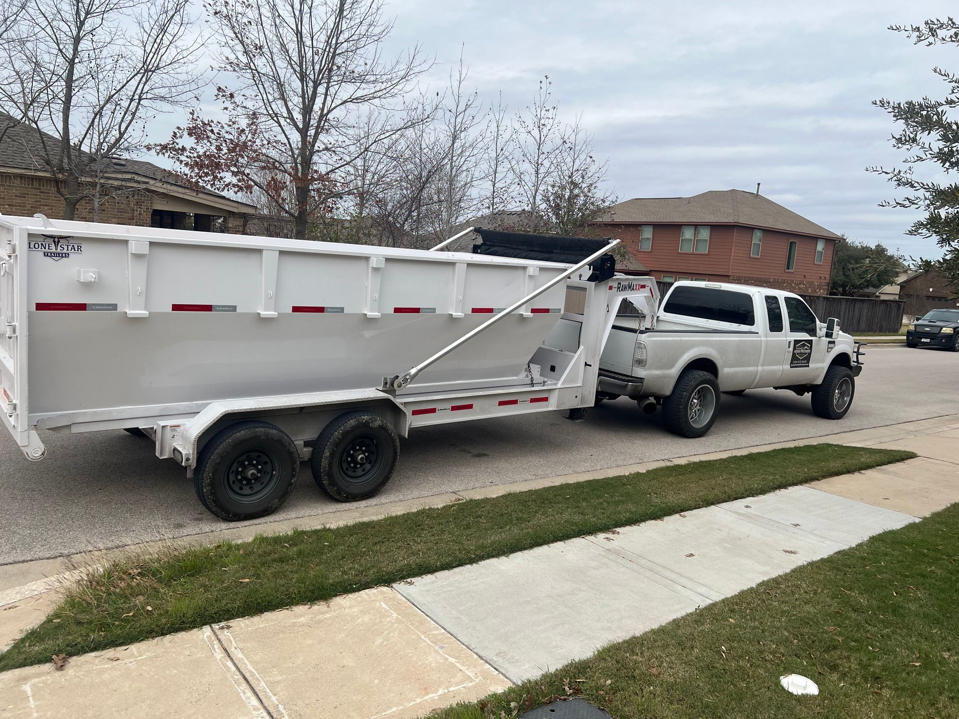 A white truck with a trailer attached to it is parked in a dirt field.