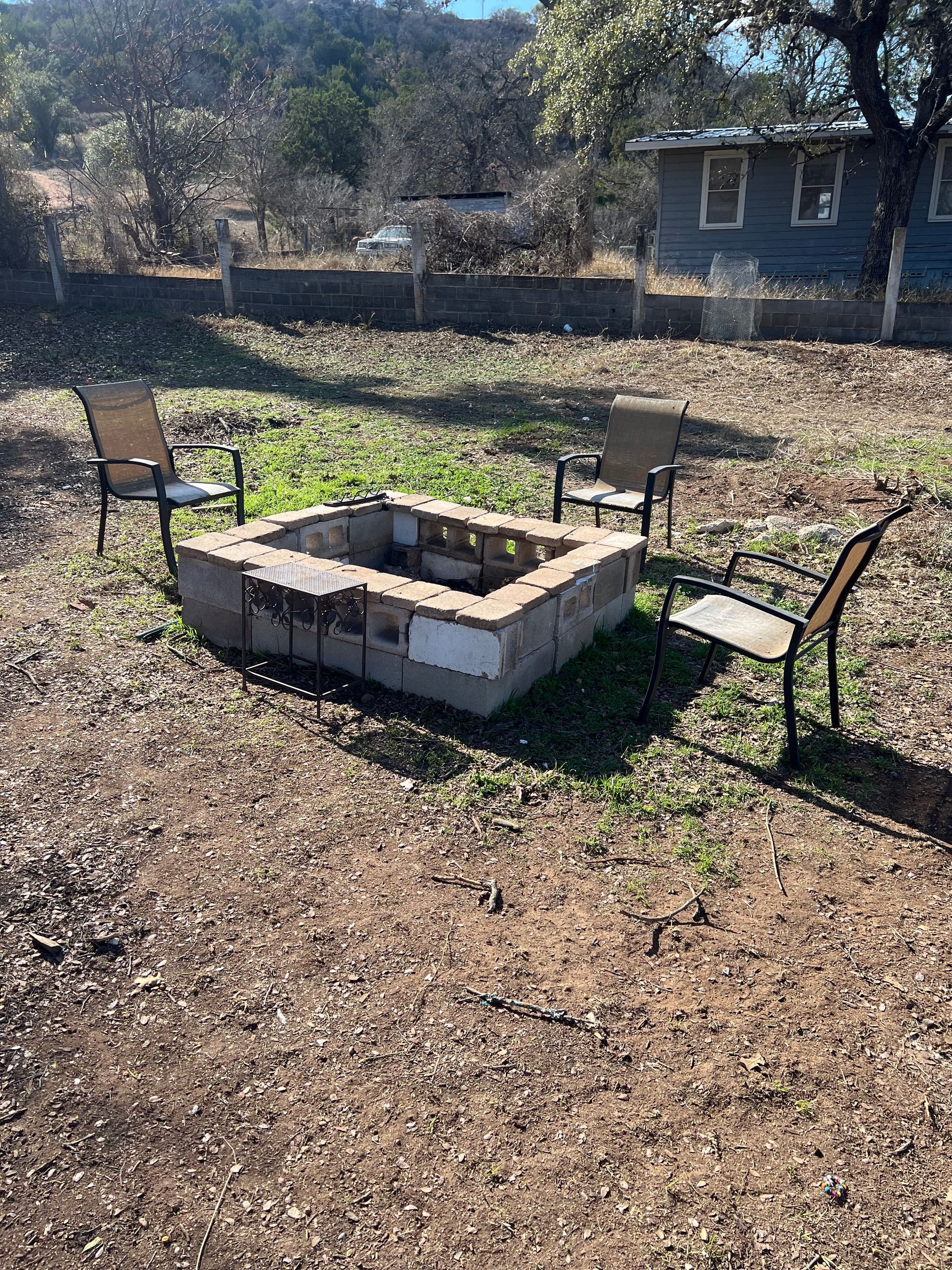 A fire pit in the middle of a dirt field with chairs around it.