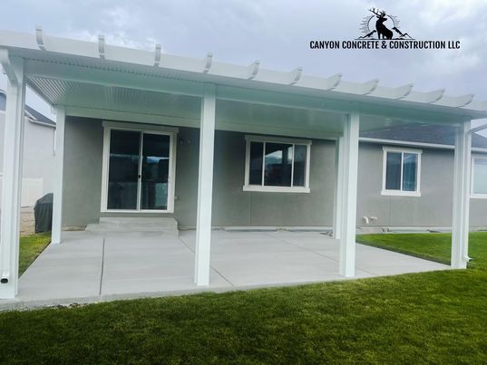 A patio with a pergola on top of it in front of a house.