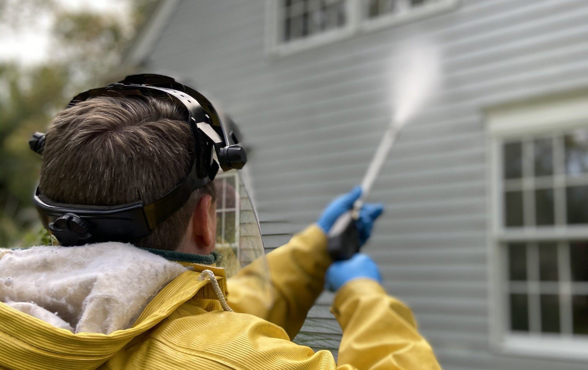 Man wearing PPE and power washing the vinyl siding of a home