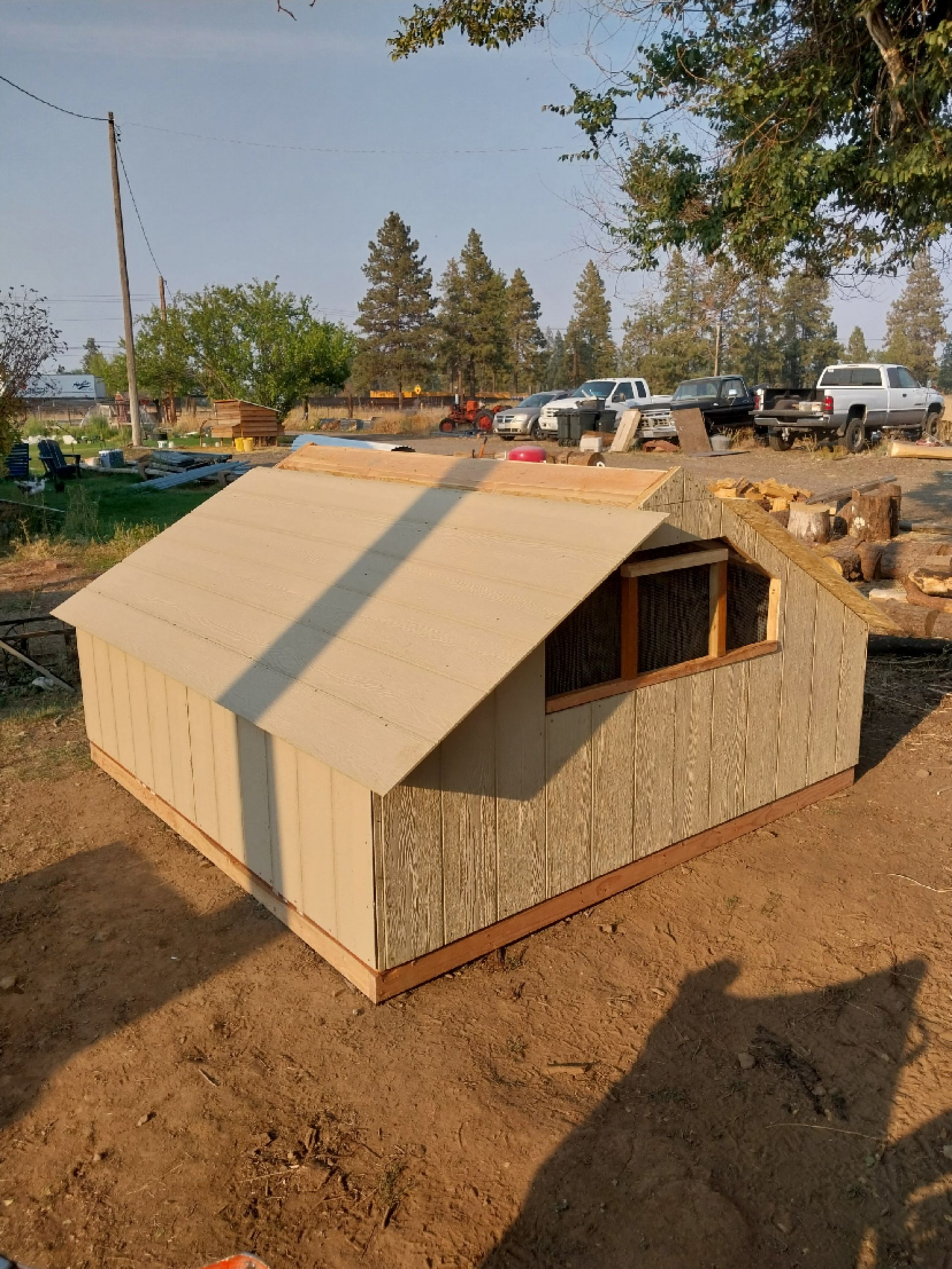 A partially built shed with a slanted roof, brown siding, and a small window outdoors.