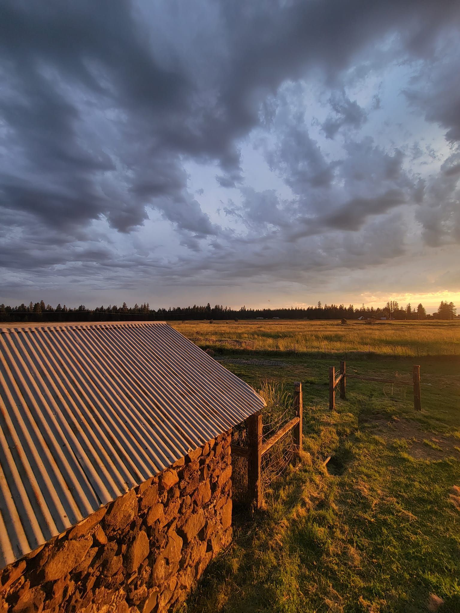Stone shed in a field under a dramatic, cloudy sky at sunset.