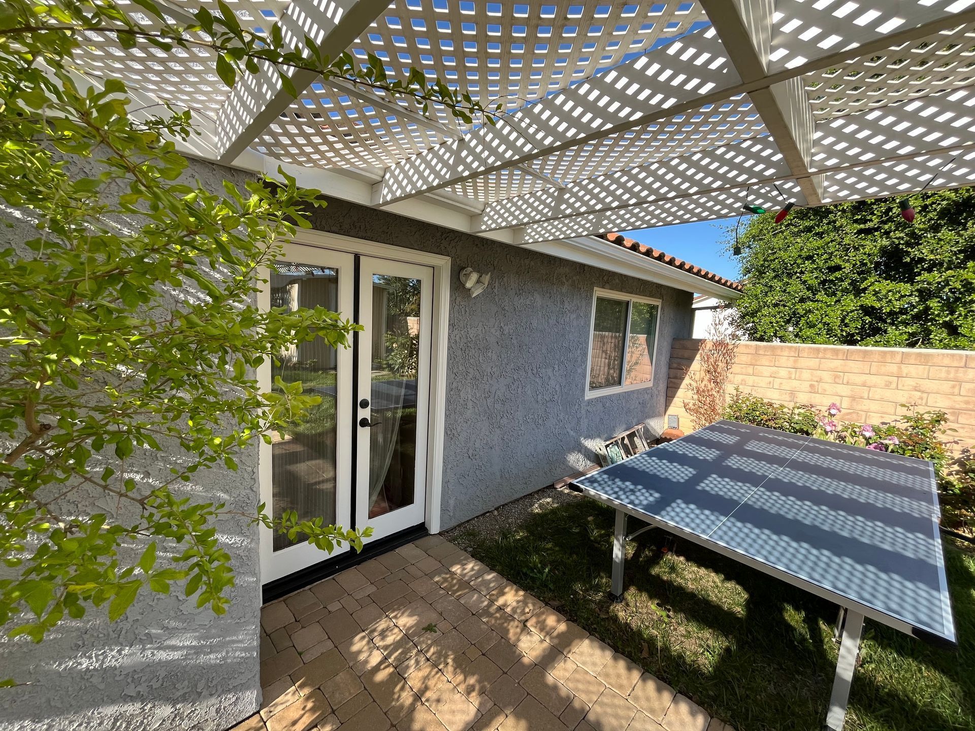 A patio with a table and a pergola in the backyard of a house.
