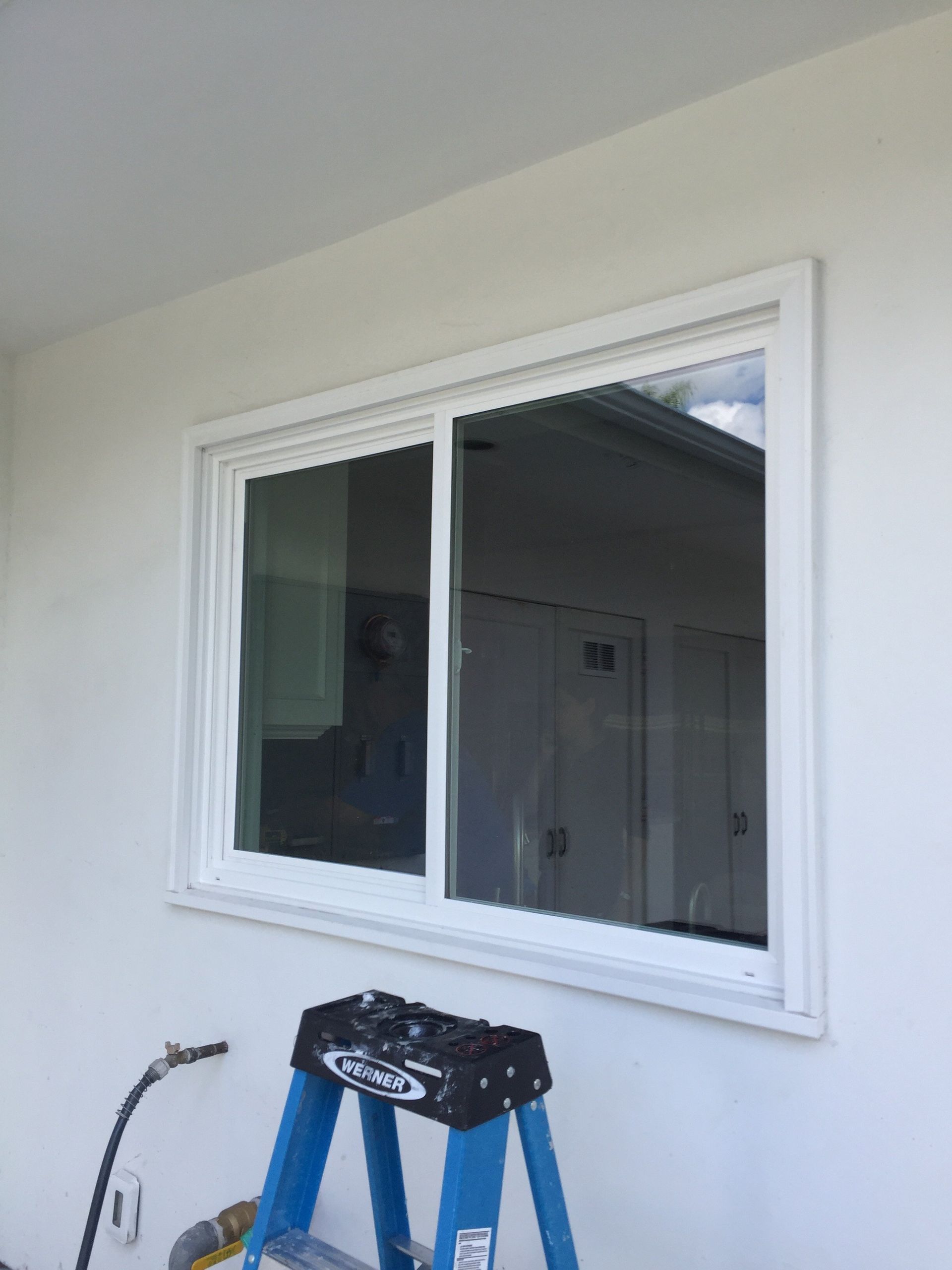 A blue ladder is sitting in front of a window on a white wall.