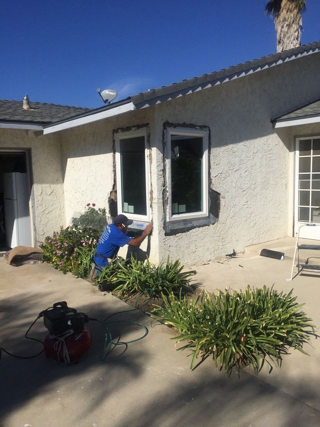 A man is installing a window on the side of a house.