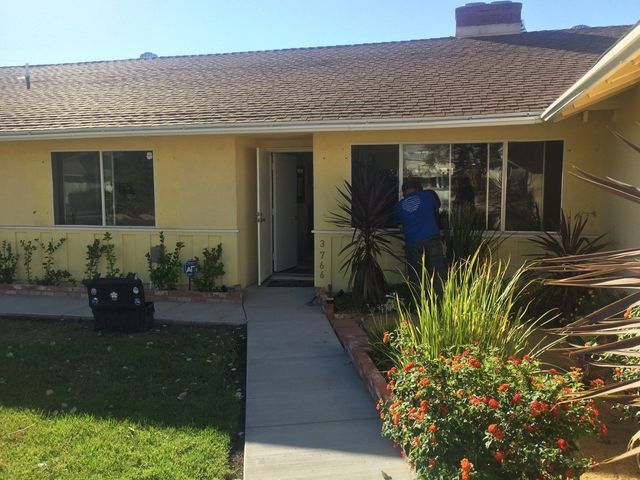 A man in a blue jacket is standing in front of a yellow house.
