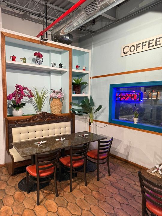 Interior of a cafe with a seating area. Table, chairs, and shelves with flowers. Blue and red accents.