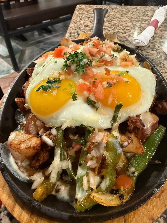 Skillet breakfast with two fried eggs, potatoes, peppers, onions, and salsa on a wooden board.