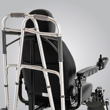 Folded silver walker strapped to a black wheelchair against a light gray background