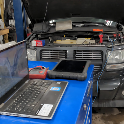 Rb Garage - A laptop is sitting on a blue table in front of a car with the hood open