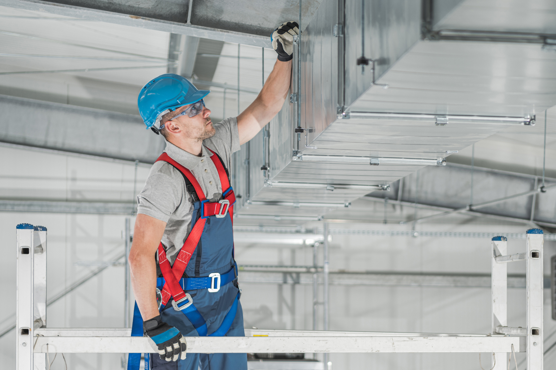 A man is working on the ceiling of a building while standing on a ladder.