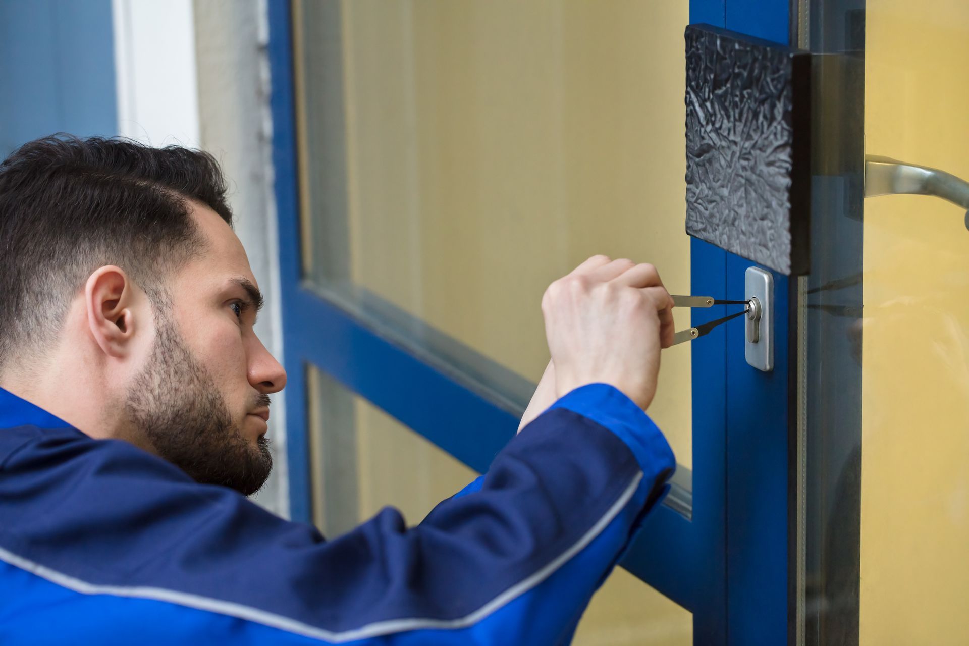 Close-up of an emergency locksmith, in a blue uniform, opening a door with a lock picker.