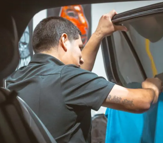 Man opening a car trunk, holding the lid with both hands. He is wearing a black shirt.