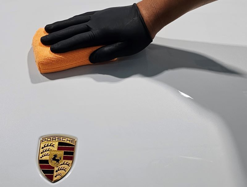 Gloved hand with orange cloth polishing a white Porsche.