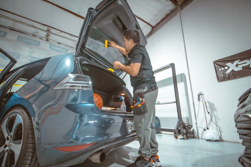 A man is applying window tinting to a car in a garage.