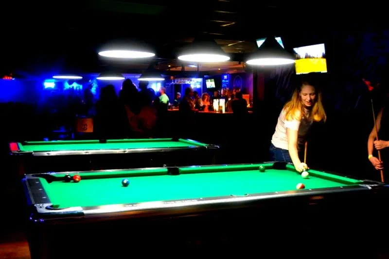 A woman is playing pool in a pool hall.