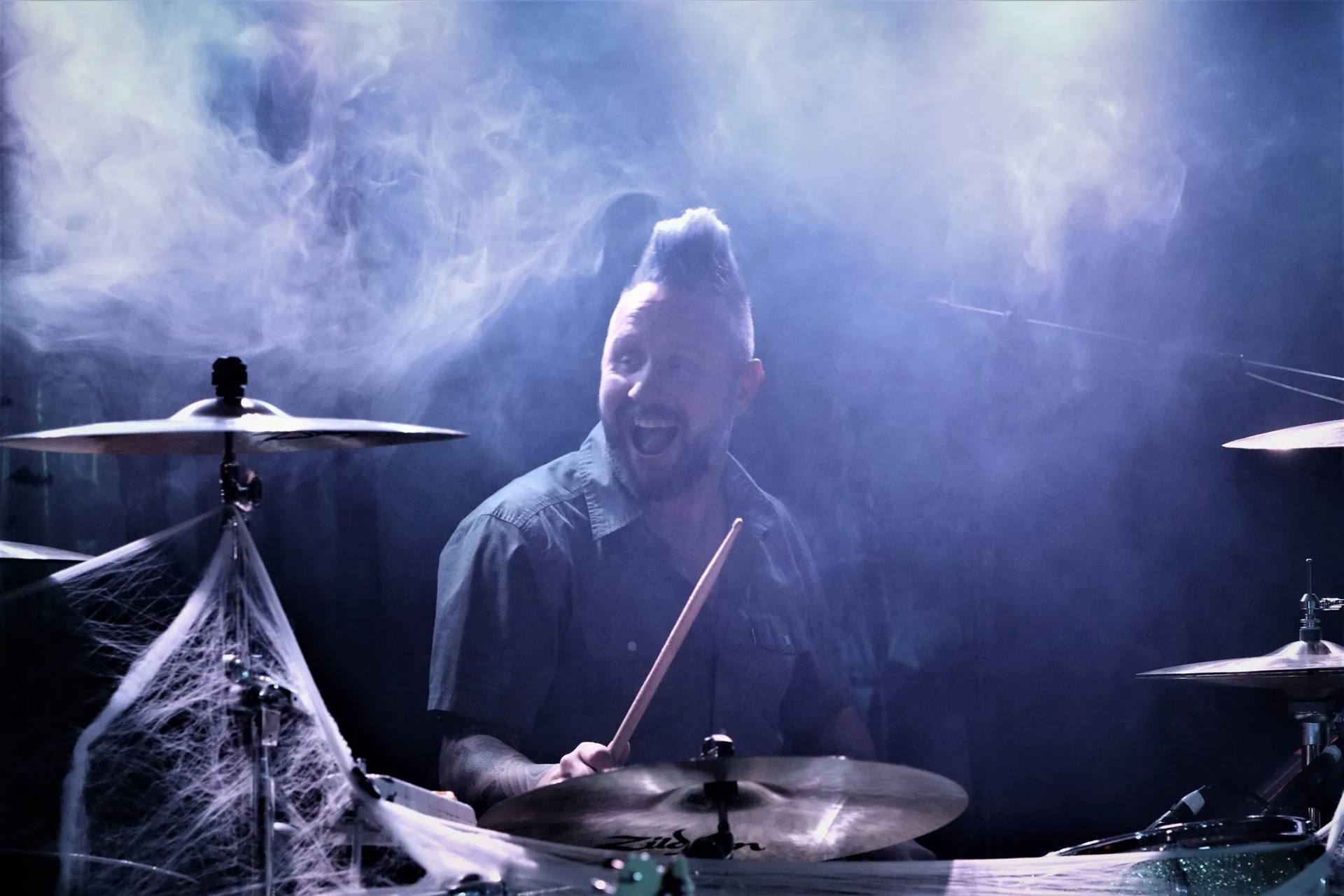 A man with a mohawk is playing drums in a dark room.