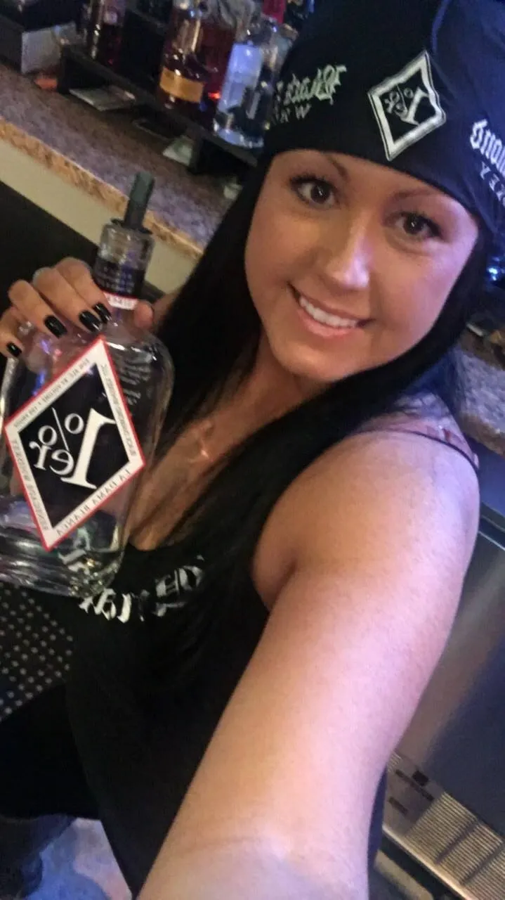 A woman wearing a bandana is holding a bottle of alcohol