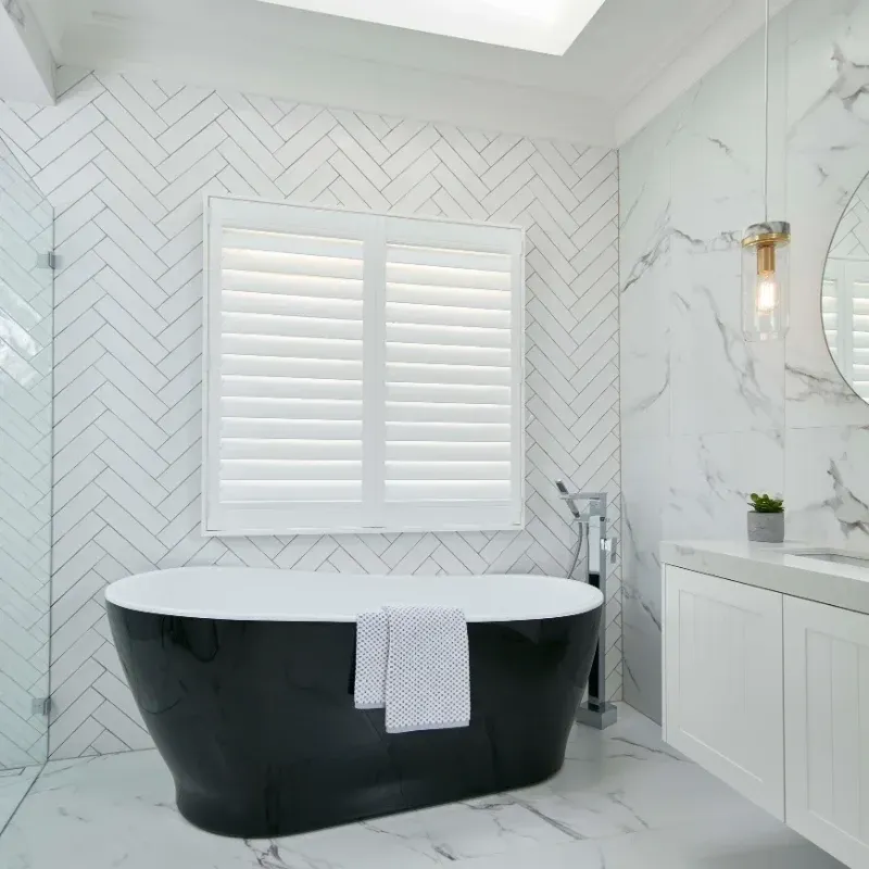 Modern bathroom with black tub, white shutters, marble walls and floor.