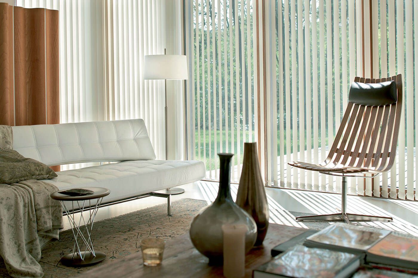 Living room with a white sofa, wooden chair, and large windows with vertical blinds.