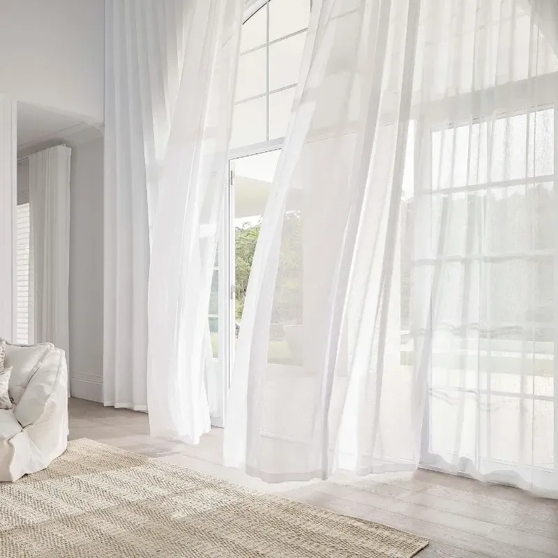 White sheer curtains billowing in front of a window, a room with a rug and a sofa.