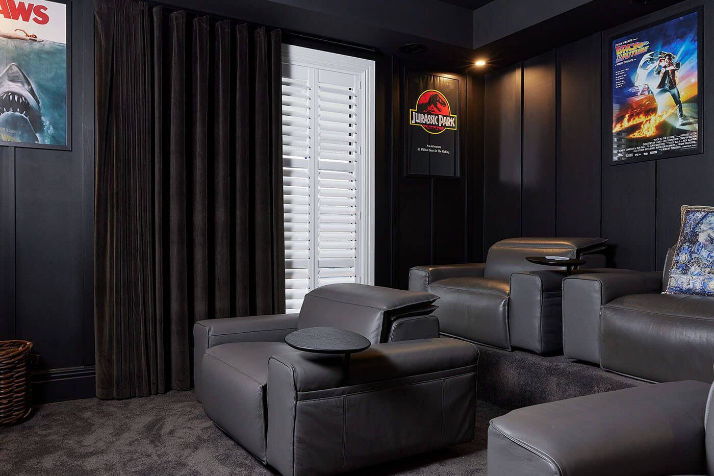 Dark home theater with gray reclining chairs, movie posters, and dark curtains.