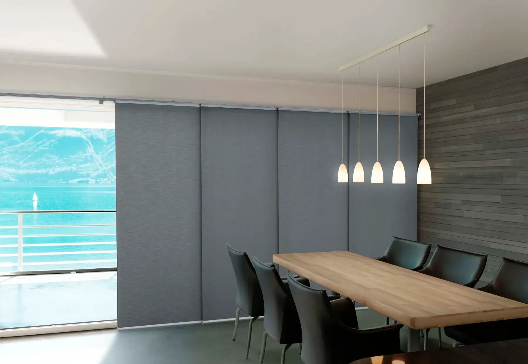 Dining room with sliding panel shades, wooden table, and pendant lights.