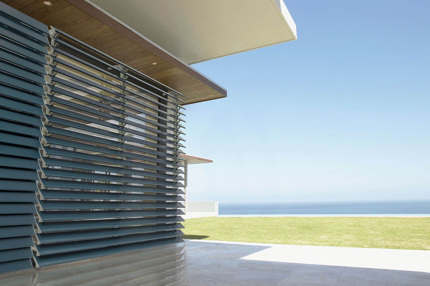 Modern building exterior with blue horizontal slats, overlooking ocean and grass.