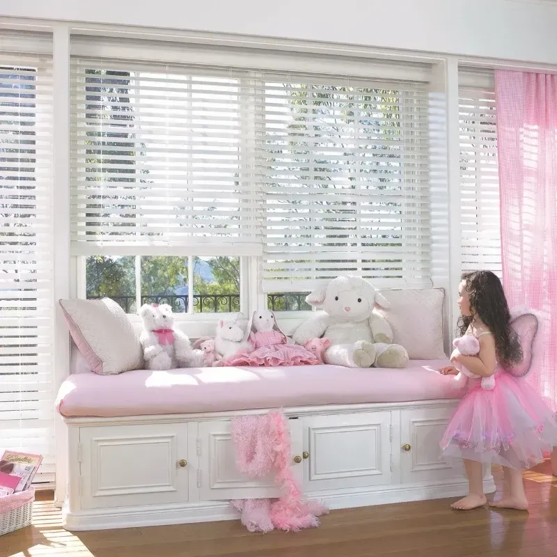 A girl in a pink tutu stands by a window seat with plush toys.