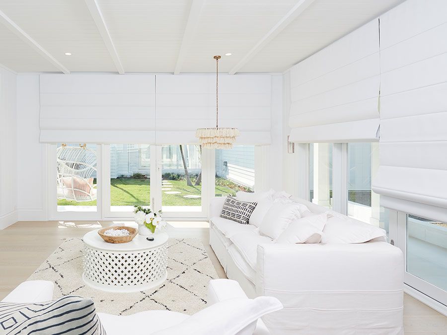 White living room with bright sunlight, white furniture, and a patterned rug.
