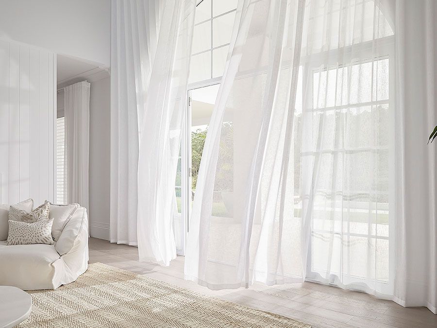 White sheer curtains blowing in front of a large window, bright natural light, minimalist living room.
