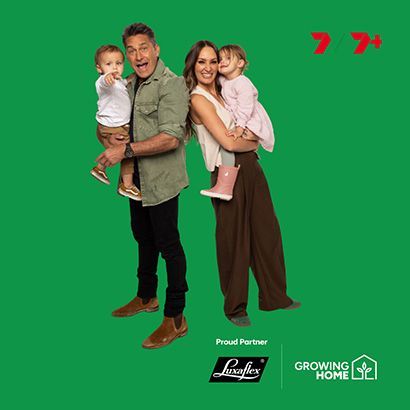 A family of four poses on a green background. The parents hold a toddler each.