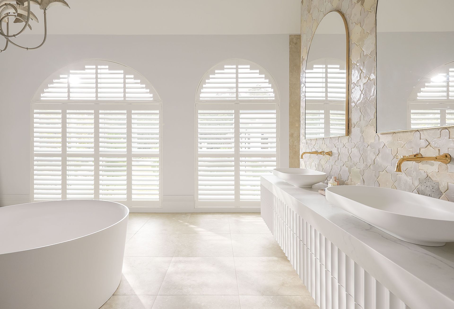 Elegant white bathroom with arched windows, soaking tub, and double sinks.