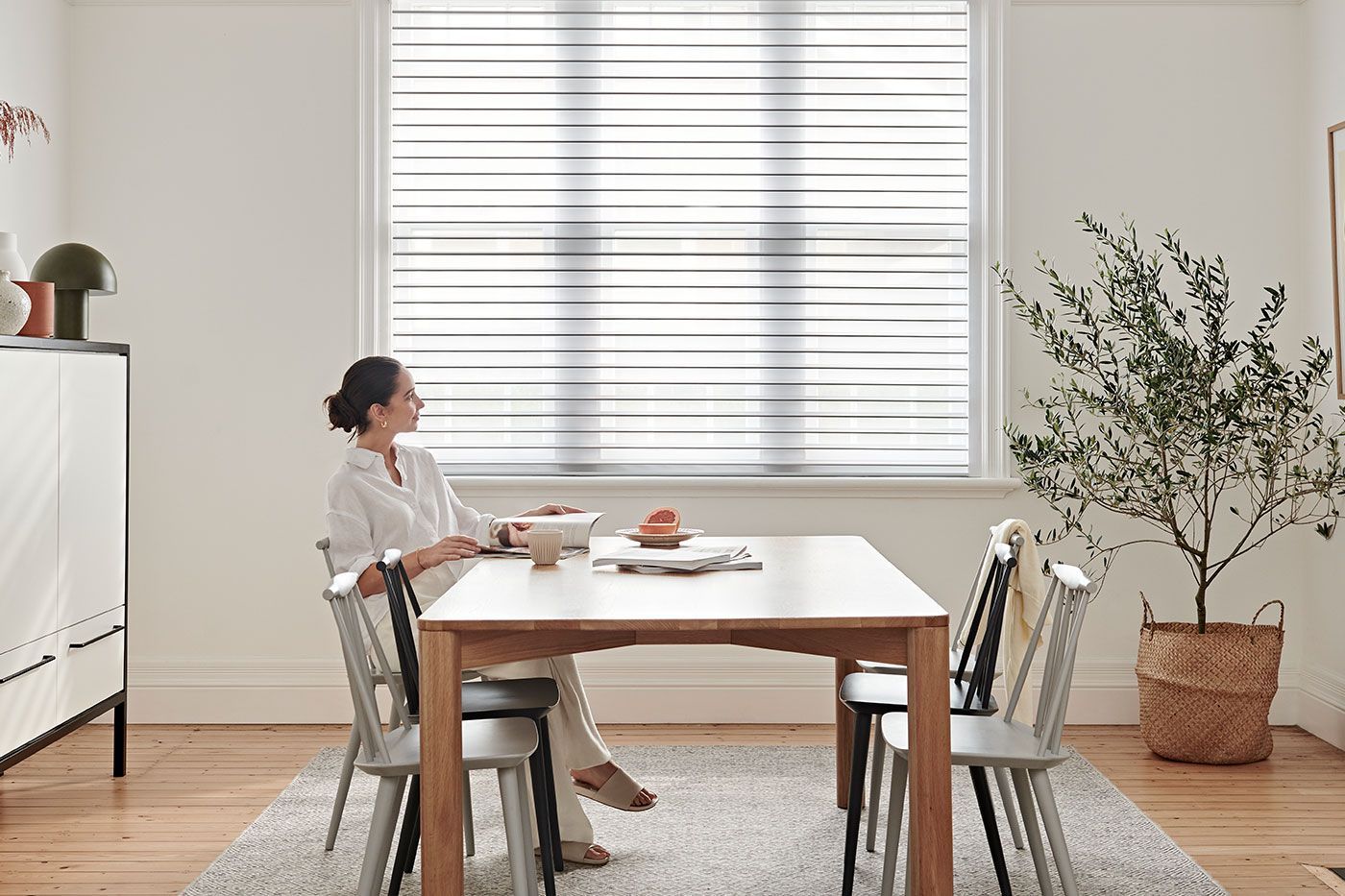 A bright room with a large white potted plant, folding shutters, and a rustic wooden table.